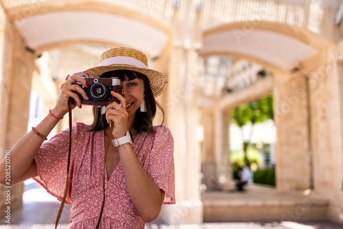 Konstfotografi Close-up of a dark-haired woman holding a vintage camera near her face, looking through the viewfinder with focused expression