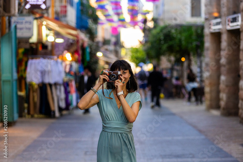 Obraz na płótnie Close-up of a dark-haired woman holding a vintage camera near her face, looking through the viewfinder with focused expression