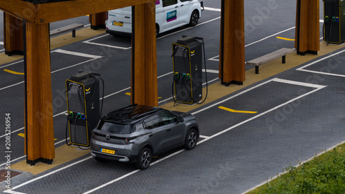 Muiden, Netherlands - 11 June 2026: Aerial view of the Fastned charging station with a grey car parked at a charging point, featuring wooden pillars and modern EV infrastructure.