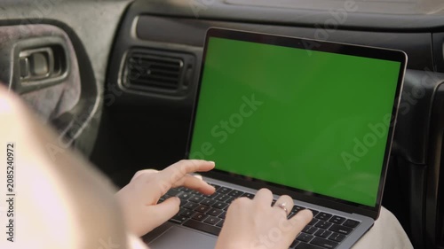 Person types on laptop with green screen inside car. Hands move actively over keyboard. Focus stays on screen and typing motion. Ideal for remote work, digital meetings, or travel content