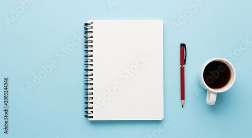 Notebook pen and coffee cup arranged on a light blue surface.