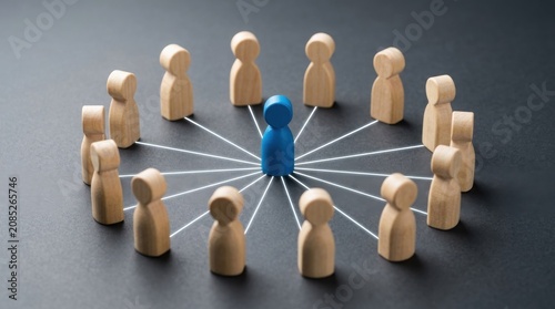 Blue wooden figure standing in a circle of connected wooden people on dark background