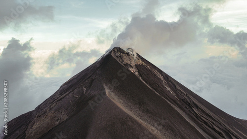 Volcán Fuego emits a plume of smoke above the mountains of Guatemala during a period of volcanic activity under clear skies.