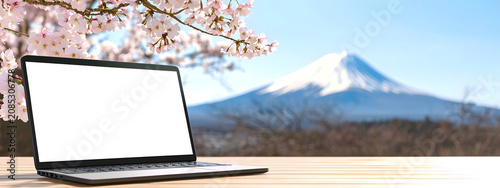 A laptop with a white screen mockup next to cherry blossoms against a distant volcano