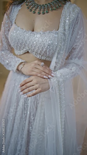 Close-up detail shot of a bride's hands clasped together over an intricately sequined and pearl-beaded silver-grey blouse, showing a diamond engagement ring, thin bracelet, manicured nude nails