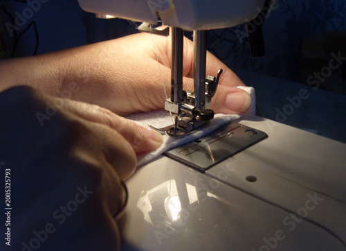 Foto A close-up shot of a seamstress's hands guiding white fabric under the needle of an electric sewing machine