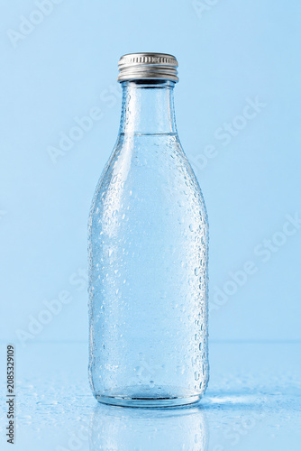 Clear glass water bottle with tiny dew droplets against light blue background