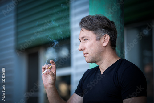 Bild auf Leinwand Man smoking a cigarette outdoors, looking away with a thoughtful expression