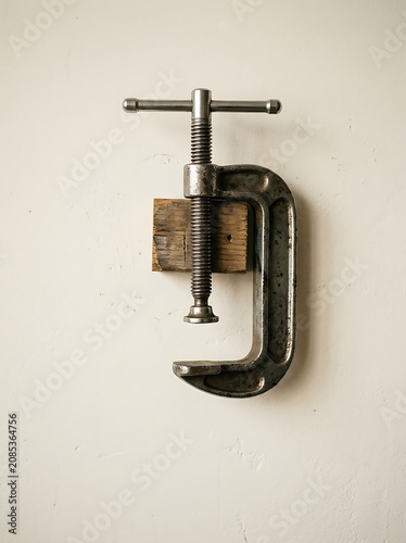 Vintage Metal C-clamp Holding a Small Wood Block Against a Textured Wall
