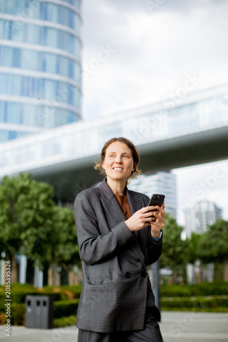 Businesswoman using smartphone in a city park near modern buildings in daytime