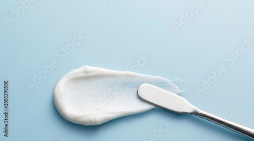 A smooth white cosmetic cream smear spread with a metal spatula on a clean light blue background for skincare product