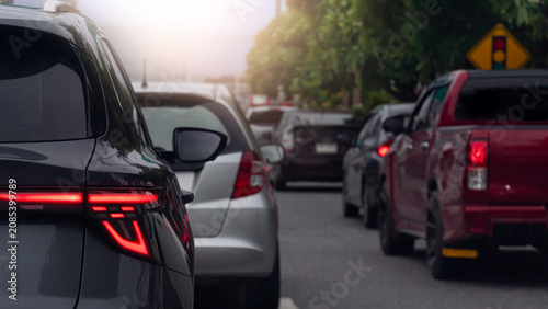 Vehicles gridlocked in heavy traffic on an urban highway. Red brake lights flare across the long rows of cars during a busy evening sunlight is soft commute. Side road with trees pleasant atmosphere.