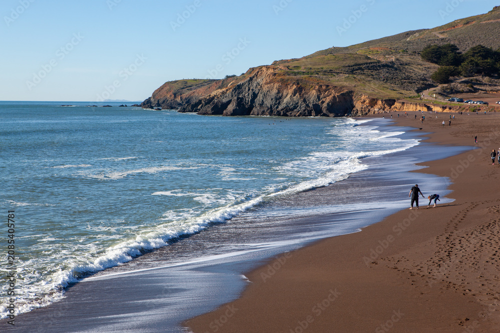 Obraz premium A father and child play on the sandy shore of Rodeo Beach, Marin Headlands, California, USA, enjoying a sunny day by the Pacific Ocean.