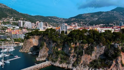 Aerial orbit around Monaco Cathedral and the old town on the Le Rocher cliff above Port de Fontvieille, with moored sailboats, Monte Carlo towers and mountains of the French Riviera behind.