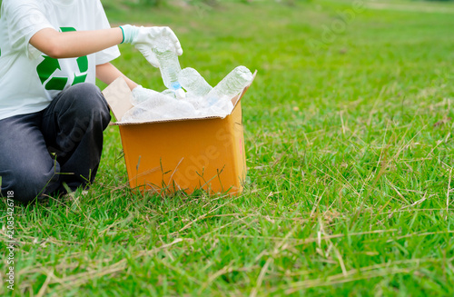 Volunteer collecting plastic bottles for recycling in a green park. Sustainable waste management, environmental cleanup, circular economy, and eco-friendly community action.
