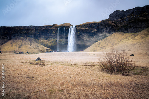 people visit Seljalandsfoss, one of Iceland's most famous waterfalls south of Reykjavik, on a cloudy day.