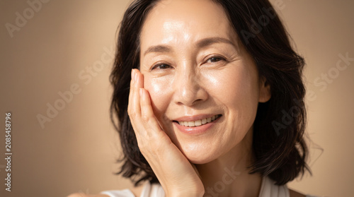 Mature Asian woman with glowing skin smiling and touching cheek
