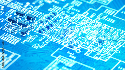 Blue electronic circuit board close up with tiny components, fine pathways, and glowing cyan light. Technology background for hardware, data, engineering, and digital design projects.