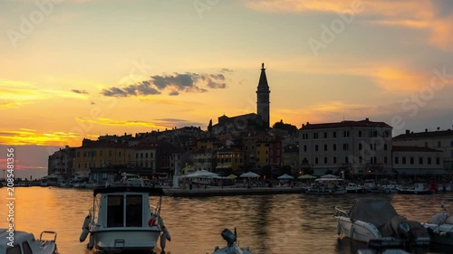 Sunset time lapse of Rovinj old town coastal skyline in Croatia featuring Church of St Euphemia bell tower, moving boats, and fading twilight sky