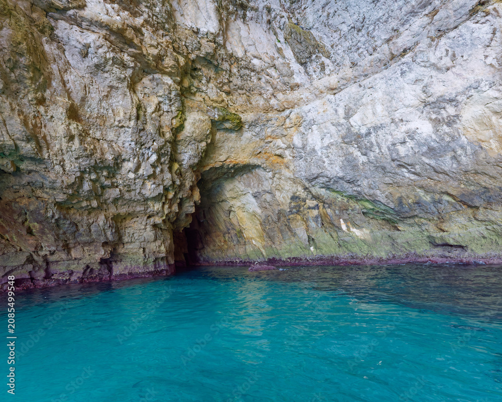 Fototapeta premium Rugged rock formation and steep limestone cliffs standing in the calm sea at Blue Grotto, Malta