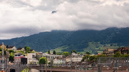 Lucerne railway station timelapse with rushing clouds engulfing Mount Pilatus peak, train yard and alpine foothills, Switzerland