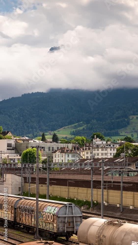 Time lapse of rushing clouds over Mount Pilatus peak and Lucerne railway tracks with cargo trains, dramatic alpine landscape in Switzerland