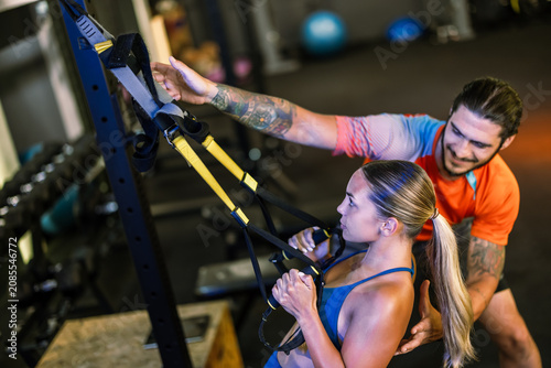 Fitness trainer assisting a young woman with her posture during a suspension strap workout