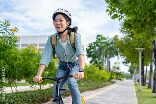 Asian female employee rides a bicycle on a nature road. She is happy and wears headphones listening to her favorite music.