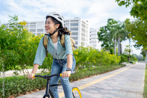 Asian businesswoman wears a helmet and headphones listening to her favorite music while cycling to work on a bright new morning.