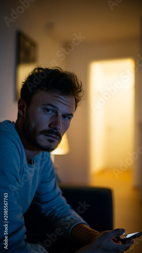 Concerned Man Holding Smartphone While Looking Toward Open Door at Night