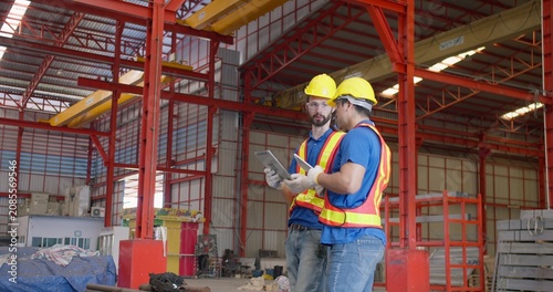 Obraz na plátně Two industrial workers collaborating on site management, inspecting project details on a digital tablet inside a large steel fabrication factory