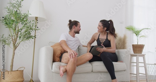 Obraz na płótnie Happy young couple relaxing on a couch using a digital tablet for online shopping or entertainment, enjoying their weekend downtime together in a modern home