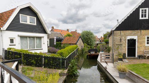 Bild auf Leinwand Canal house and wooden boat beside flower-filled garden in Hindeloopen, Frieslan