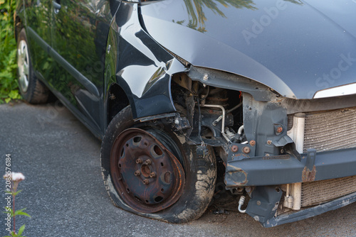 Front end of a damaged black car with severe crash damage exposing radiator and frame