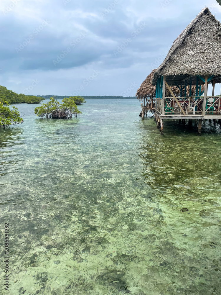 Fototapeta premium Thatched hut on wooden stilts over clear Caribbean waters near Bocas del Toro, Panama. Cloudy tropical sky