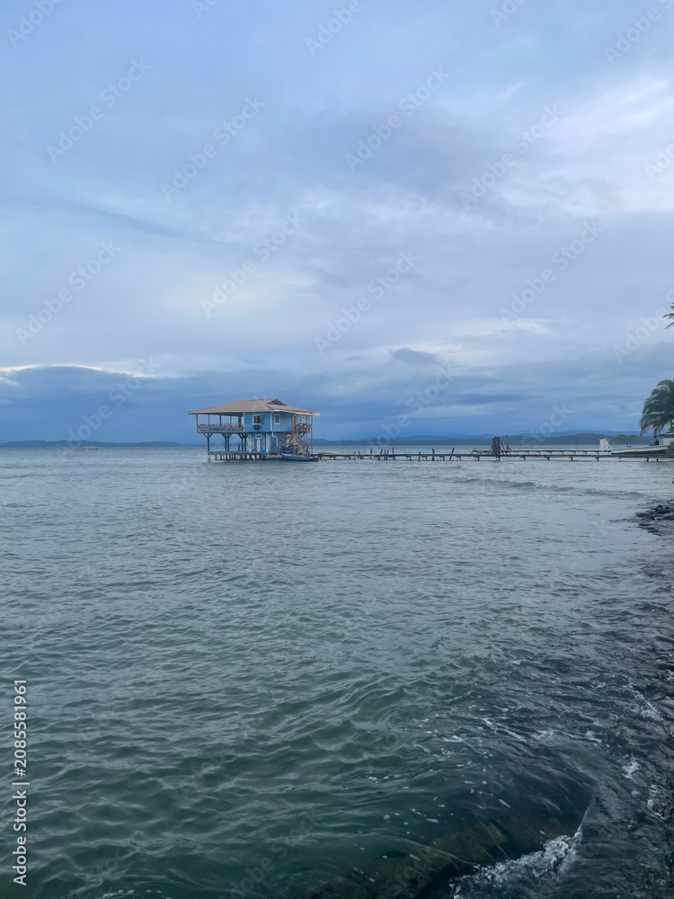 Fototapeta premium Wooden stilt house stands above calm Caribbean waters near Bocas del Toro, Panama. Gentle waves, tranquil coast
