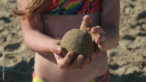Close up of child hands holding wet round sand ball on beach. Concept of creative kid summer games
