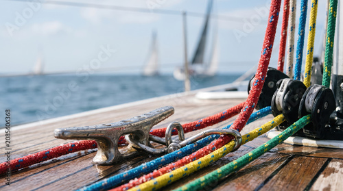 Sailboat rope cleat deck regatta colorful line rigging on wet wood with pulley and blurred yacht at sea during bright nautical race training