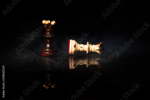 фотографія Dark chess queen standing over fallen white queen in dramatic swirling smoke on black background
