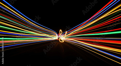 A long-exposure photograph captures streaks of vibrant light radiating from a central point. The light trails create a dynamic, abstract composition against a stark black background.