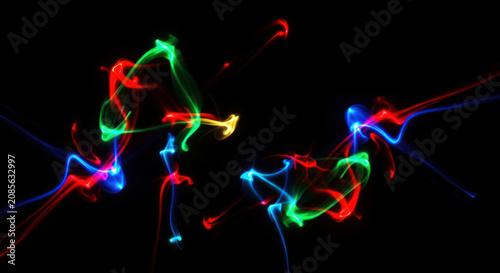 Multiple streaks of colored light dance across a black background. The light trails create abstract, flowing patterns with vibrant red, green, blue, and yellow hues.