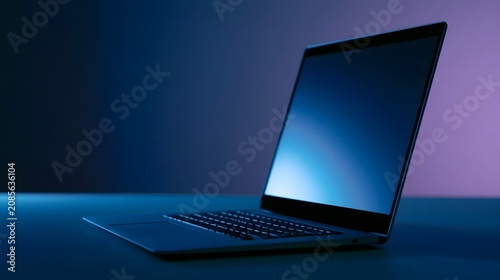 A sleek laptop computer rests on a dark surface illuminated by cool blue and purple ambient lighting