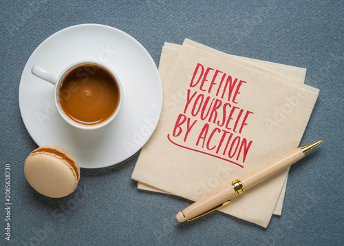 Define Yourself by Action - inspirational handwritten note on a napkin with coffee and pen, encouraging purposeful action, responsibility, and personal growth.