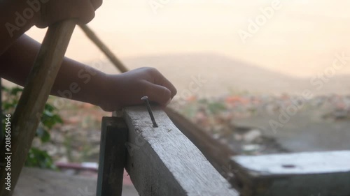 A small child's hand is holding a hammer to nail a wooden board.