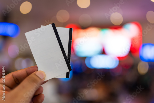 Hand holding a blank white movie ticket with bokeh background.