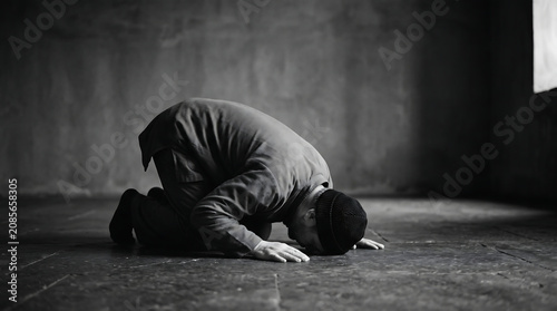 A Muslim man in prayer, head bowed in reverence on a textured floor in black and white