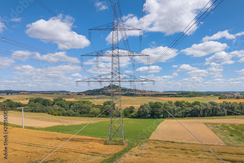 Electrical power lines are supported by a tall metal tower over a rural landscape.