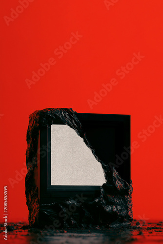 An old TV with static screen wrapped in black plastic against a solid red back