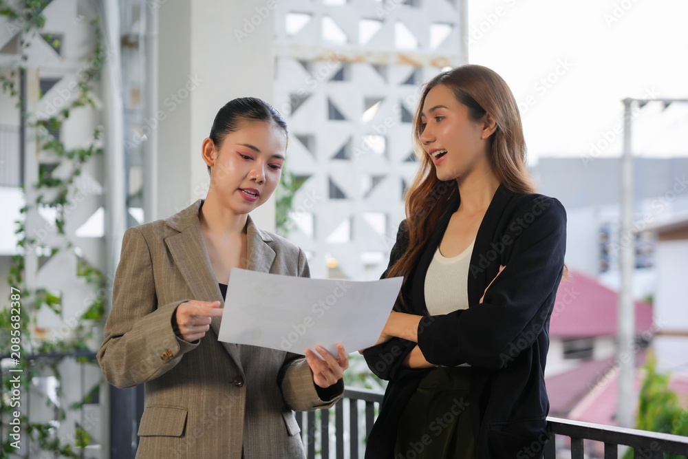 Obraz premium Asian businesswomen discussing project documents on an office balcony
