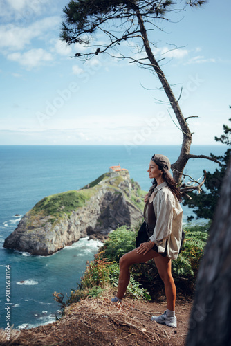 Scenic view of Gaztelugatxe island with historic hermitage, Atlantic Ocean, rugged cliffs and windswept pine tree on the northern coast of Spain.